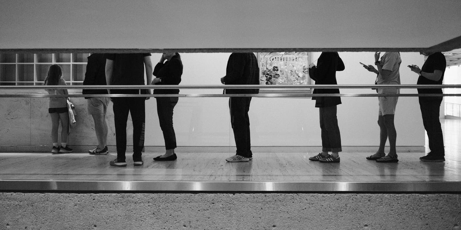People standing in a line along a railing, one of them looking at a phone