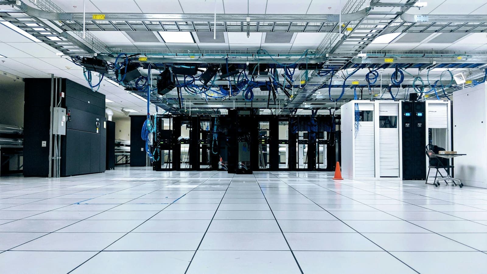 A server room with rows of racks and blue network cables running under the ceiling