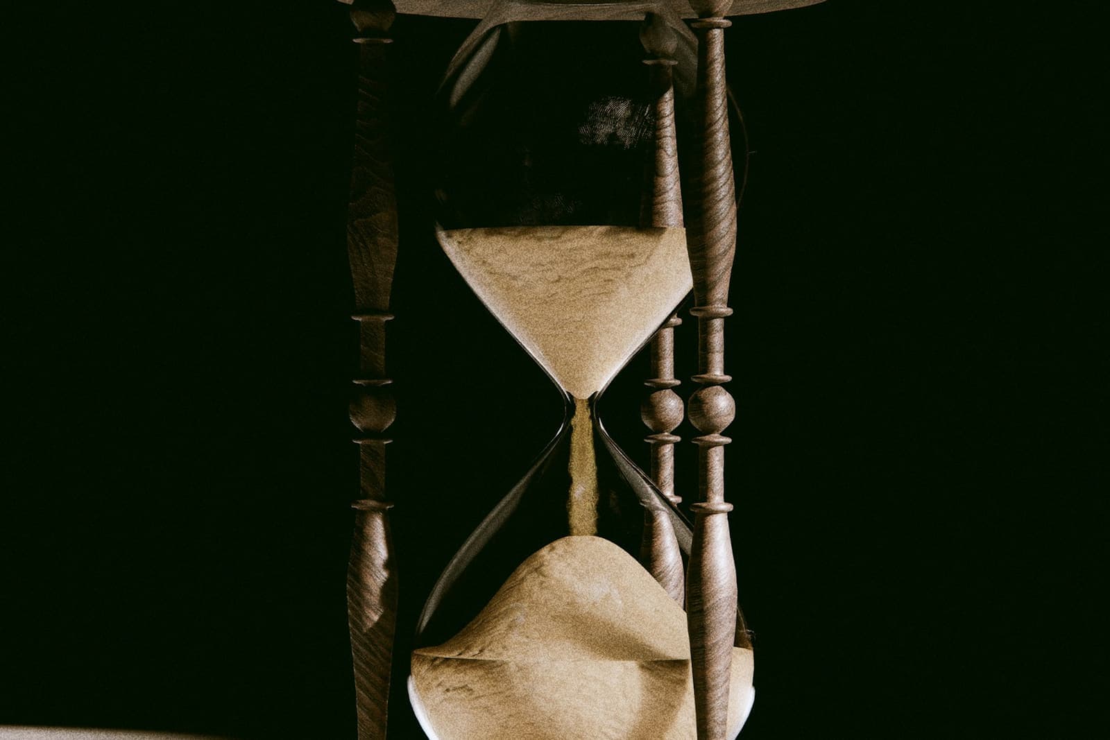 An antique hourglass with sand running through it, on a dark background