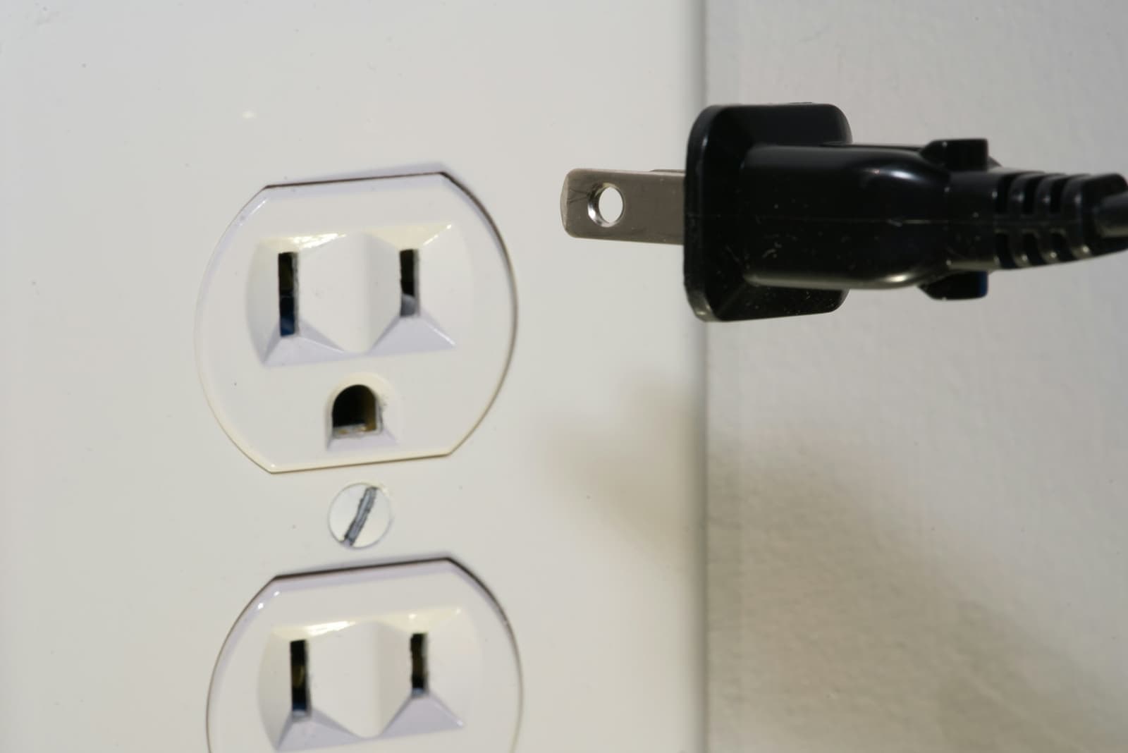 A black power plug pulled out of a white wall socket