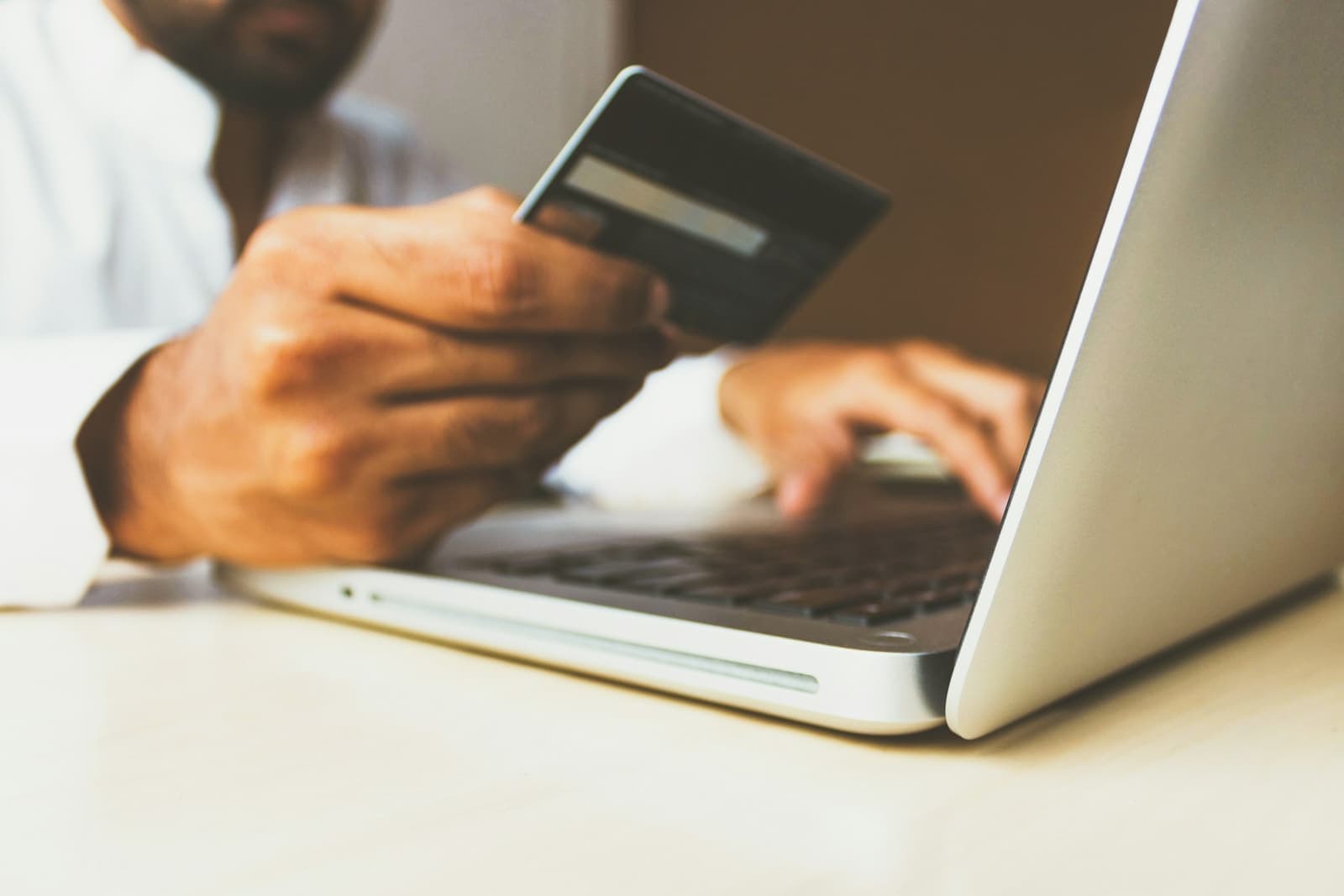 A person holding a bank card in one hand and typing on a laptop
