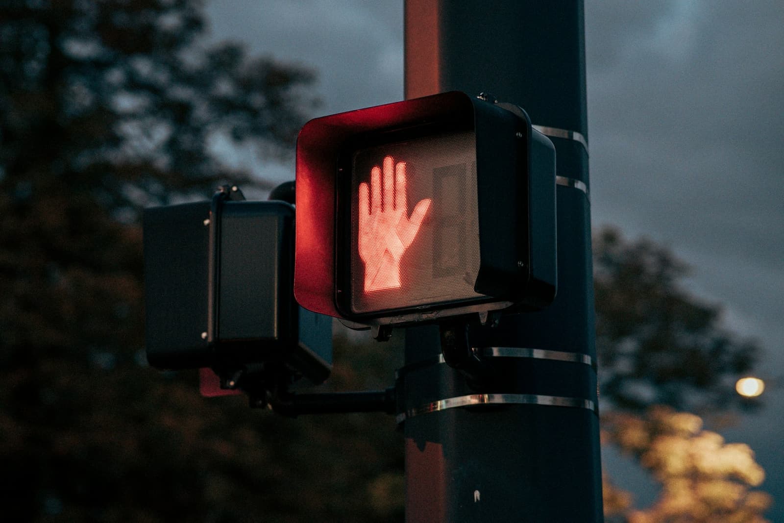 A pedestrian signal showing a red hand at dusk