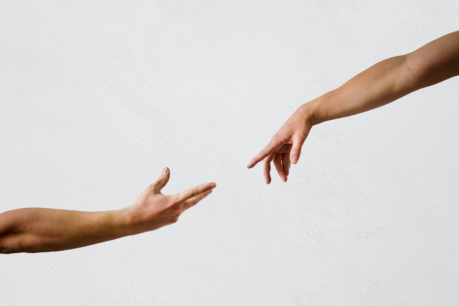 Two hands reaching towards each other against a pale wall, not quite touching